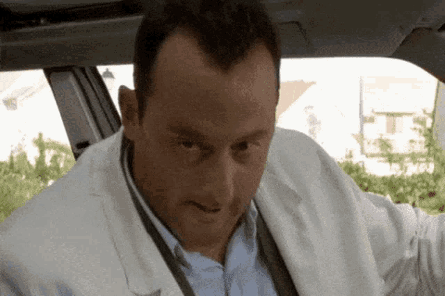 a man in a white suit is sitting in a car and looking at the camera .