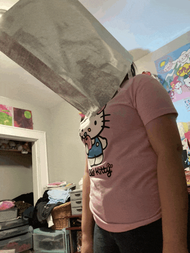 a girl wearing a pink hello kitty shirt is standing in a messy room