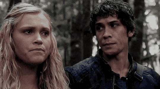a man and a woman are standing next to each other in the woods and looking at each other .