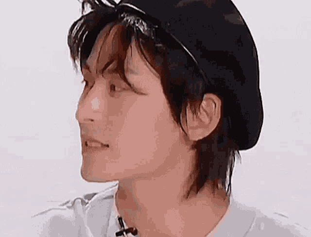 a close up of a young man wearing a black hat and a white shirt .