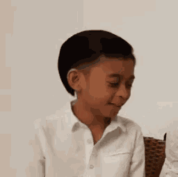 a young boy in a white shirt is sitting in a chair and looking down .