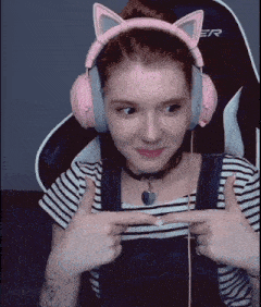 a woman wearing pink cat ears headphones is sitting in a chair and pointing at herself .