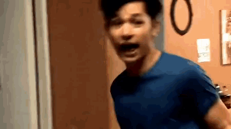 a man in a blue shirt is standing in a doorway with his mouth open .
