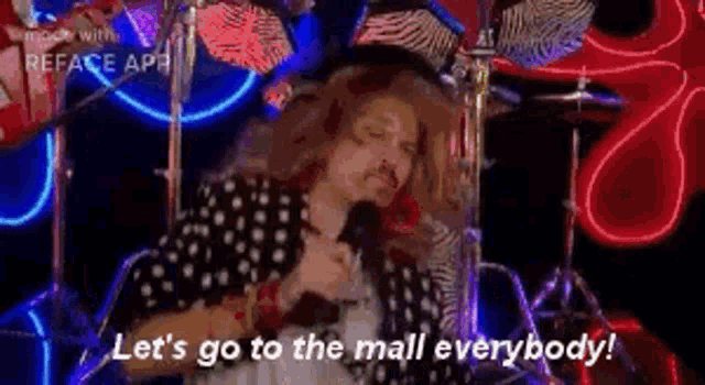 a man is singing into a microphone while standing in front of a drum set in a mall .