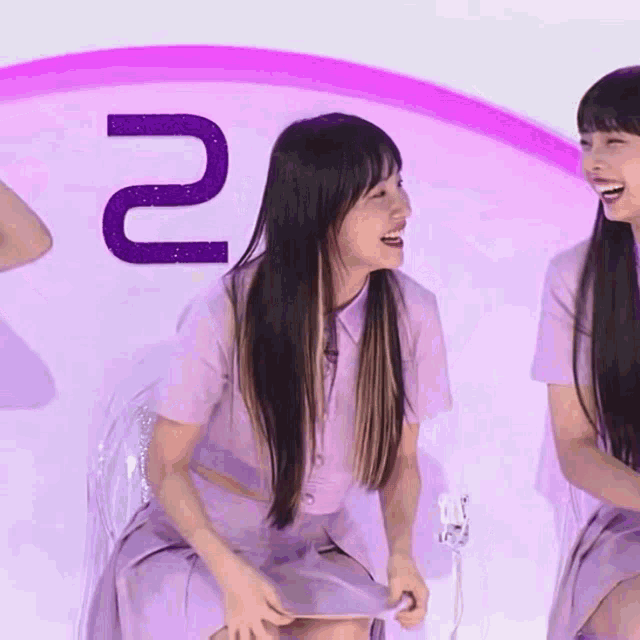 two women are sitting in front of a sign that says 2