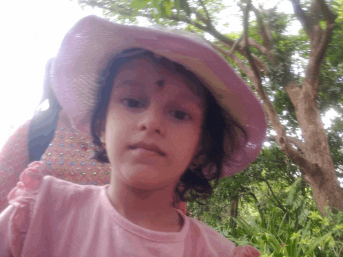 a little girl wearing a pink hat and a pink shirt looks at the camera