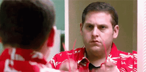 a man is looking at himself in a mirror while wearing a red shirt .