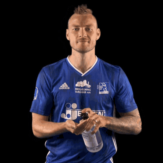 a man wearing a blue adidas jersey is holding a bottle