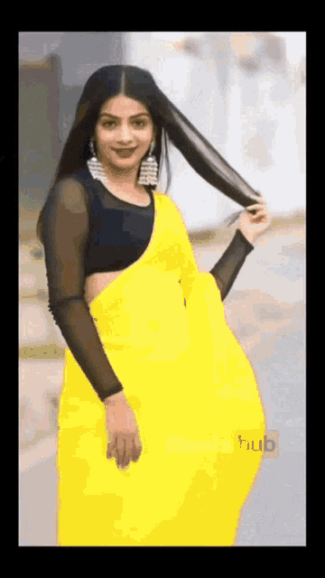 a woman wearing a yellow saree and a black blouse is holding her hair