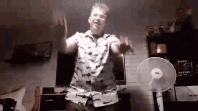 a man in a shirt is dancing in front of a fan .
