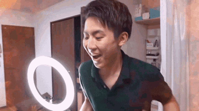 a man in a green shirt is standing in front of a ring light .