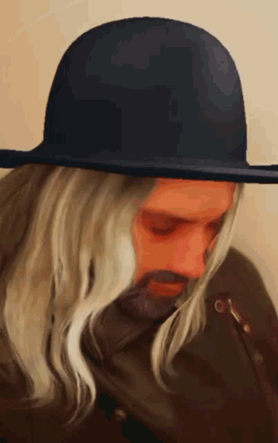 a man with long white hair and a beard wearing a black hat