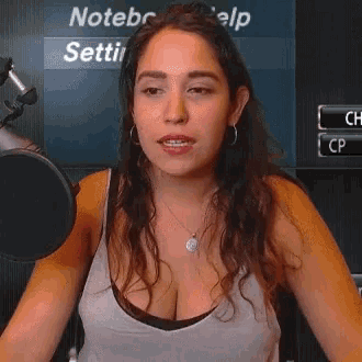 a woman stands in front of a microphone with a screen behind her that says " notebr "
