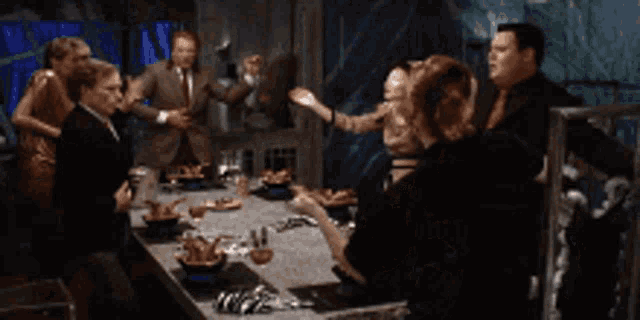 a group of people are dancing around a table with food