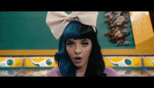 a woman with blue hair and a white bow on her head is making a surprised face .