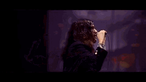 a man with long hair is singing into a microphone while standing on a stage .