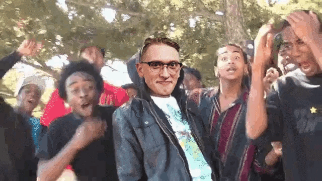 a man wearing glasses is surrounded by a group of young men