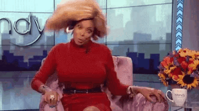 a woman in a red dress is sitting in a chair on a television show holding her hair .