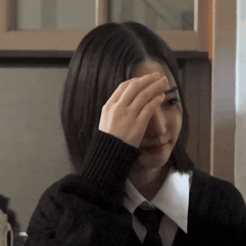 a girl in a black sweater and tie wipes her face with her hand