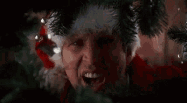 a man is wearing a santa hat and making a funny face in front of a christmas tree .
