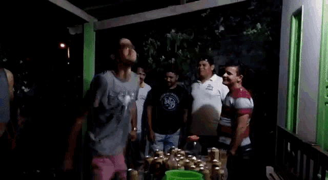 a group of men are standing around a table with beer bottles .