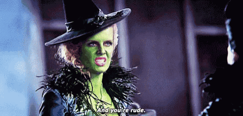 a witch with green face paint is talking to a man in a hat .