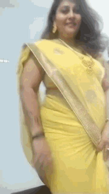 a woman in a yellow saree is dancing on a white background .