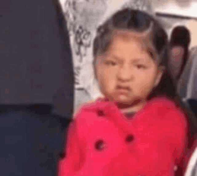 a little girl in a red jacket is making a funny face while sitting on a plane .