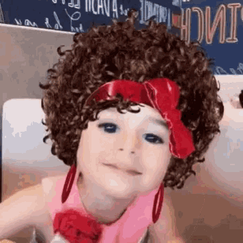 a little girl wearing a wig and earrings is smiling for the camera .