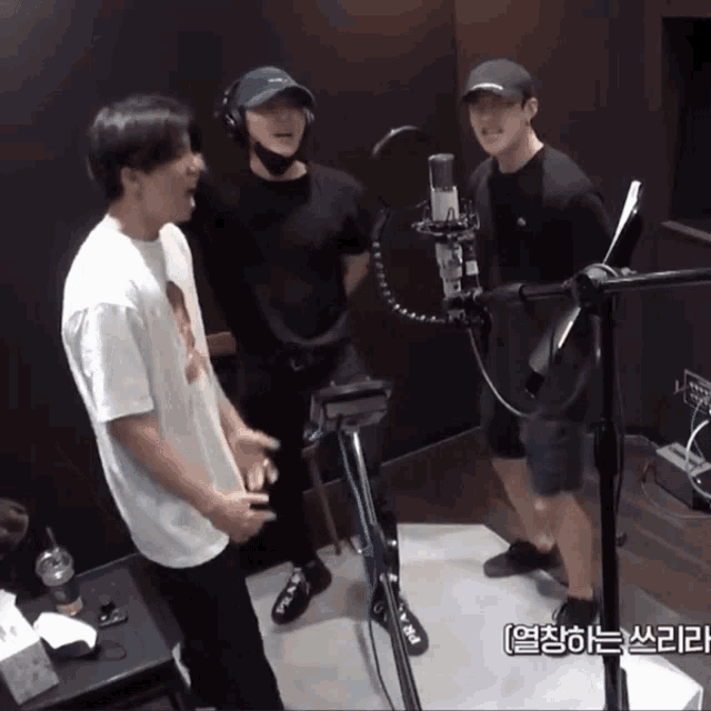 three men are singing into microphones in a room with korean writing on the wall behind them
