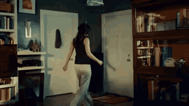 a woman is dancing in a living room next to a bookshelf .