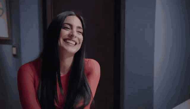 a woman in a red dress is smiling and laughing in a hallway .
