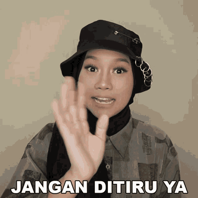 a woman wearing a hat and a hijab says " jangan ditiru ya "
