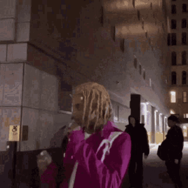 a woman in a pink coat is walking down a street at night .