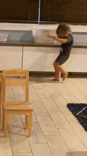a little girl is standing on a wooden floor next to a chair