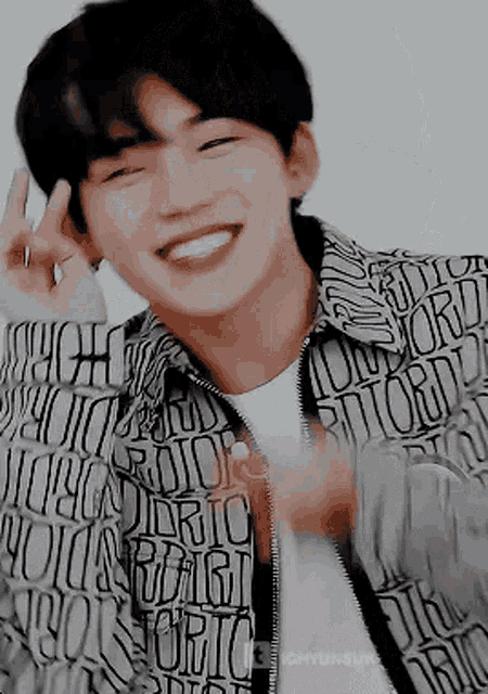 a young man is smiling and making a peace sign with his hands .