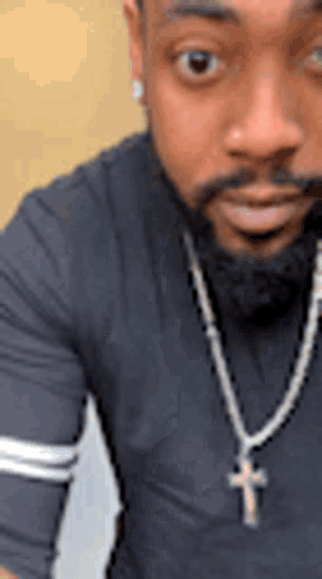 a man with a beard is wearing a black shirt and a necklace with a cross pendant .