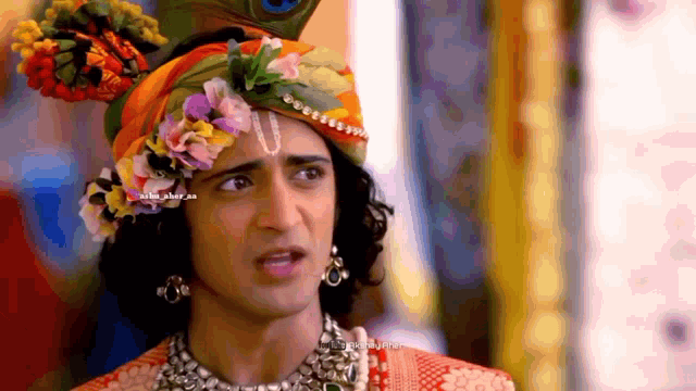 a man wearing a turban with flowers on it and a peacock feather on his head is making a funny face .