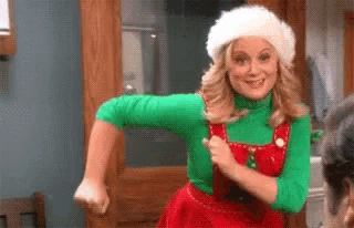 a woman is wearing a santa hat and overalls and dancing .