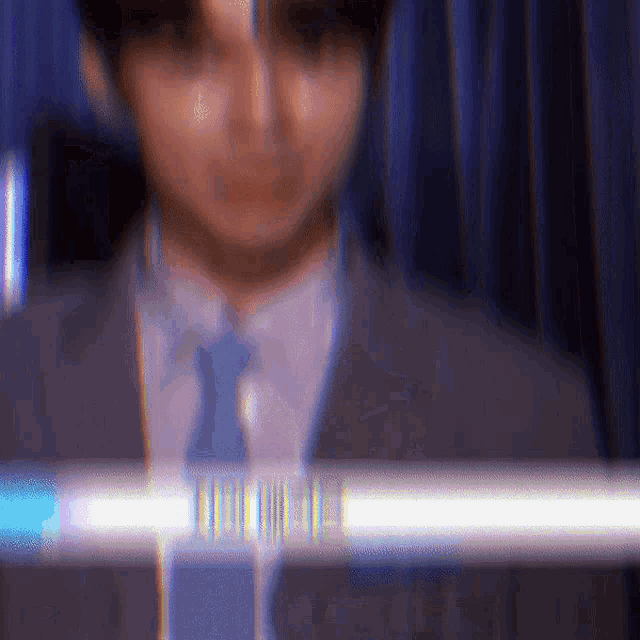 a blurry picture of a man in a suit and tie with a blue curtain behind him