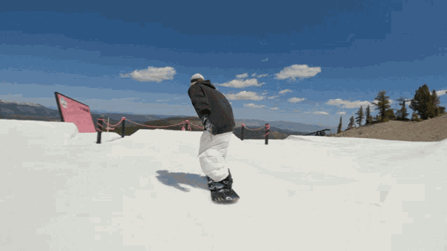 a snowboarder is doing a trick on a snowy slope with a sign in the background that says snowboarding