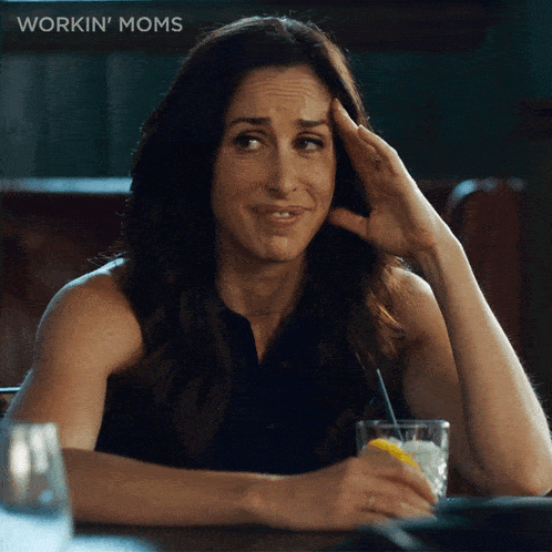 a woman is sitting at a table with a drink in her hand and the word workin ' moms is behind her