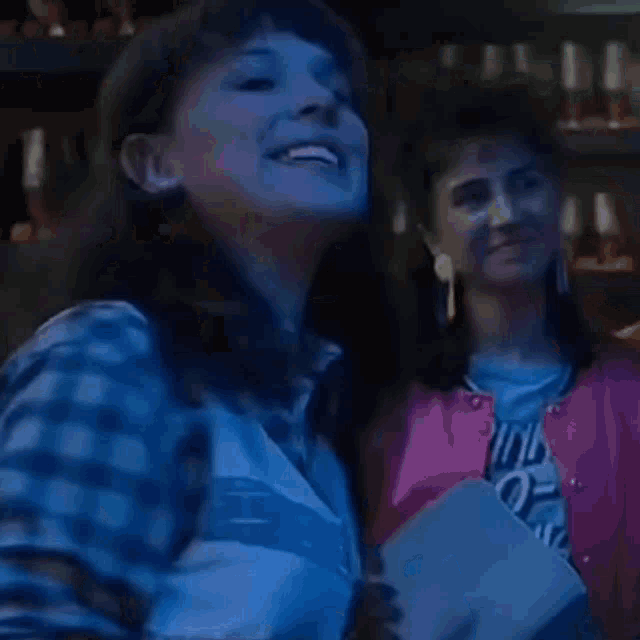 a woman in a plaid shirt is holding a piece of paper and smiling in a dark room .