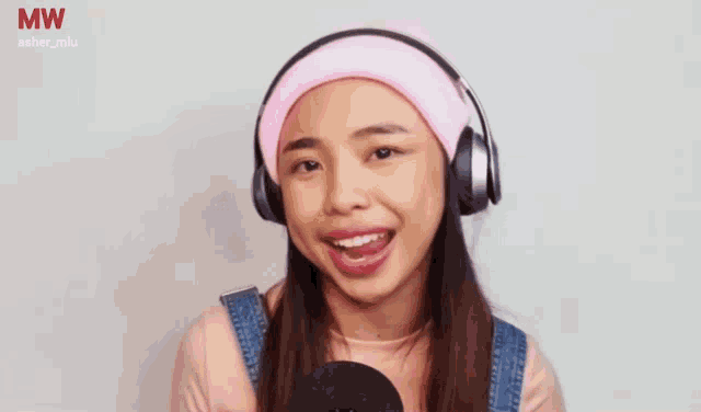 a woman wearing headphones and a pink headband winks at the camera .