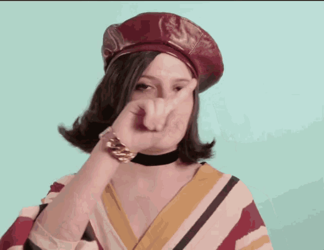 a woman wearing a beret and a striped shirt is covering her face with her hand