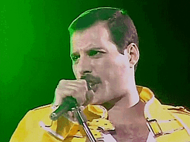a man in a yellow jacket singing into a microphone with a green background