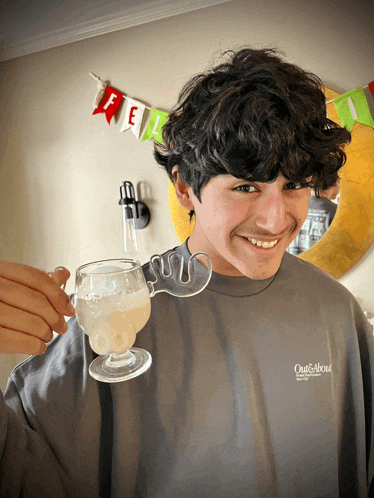 a young man wearing a grey out & about sweatshirt holds a glass