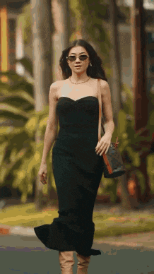 a woman in a black dress and sunglasses is walking down a street .