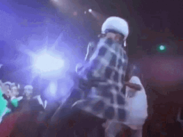 a man in a plaid shirt is dancing on a stage in front of a crowd of people .