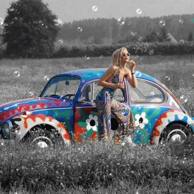 a woman blowing soap bubbles next to a colorful car in a field